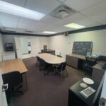 reverse photo of pilots lounge with table and chars. Small desk in background with chalk board on it